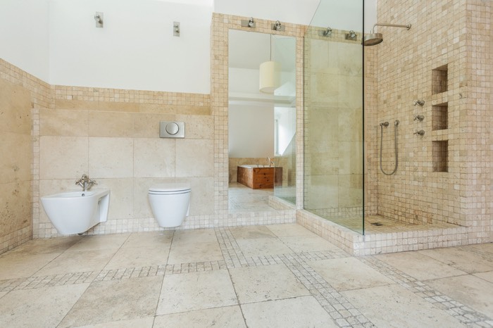 Une douche à l'italienne beige avec paroi en verre pour éclaircir la salle de bain. Salle d'eau style scandinave avec mosaïque en pierre.