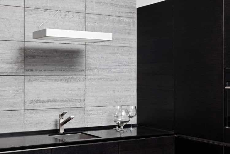 Évier encastré sous plan de travail noir. Luminaire blanc suspendue et grand carrelage mural.