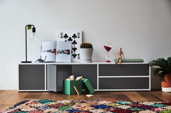 Etagère blanche et grise avec tiroirs de rangement. Parquet et tapis avec losanges multicolores.
